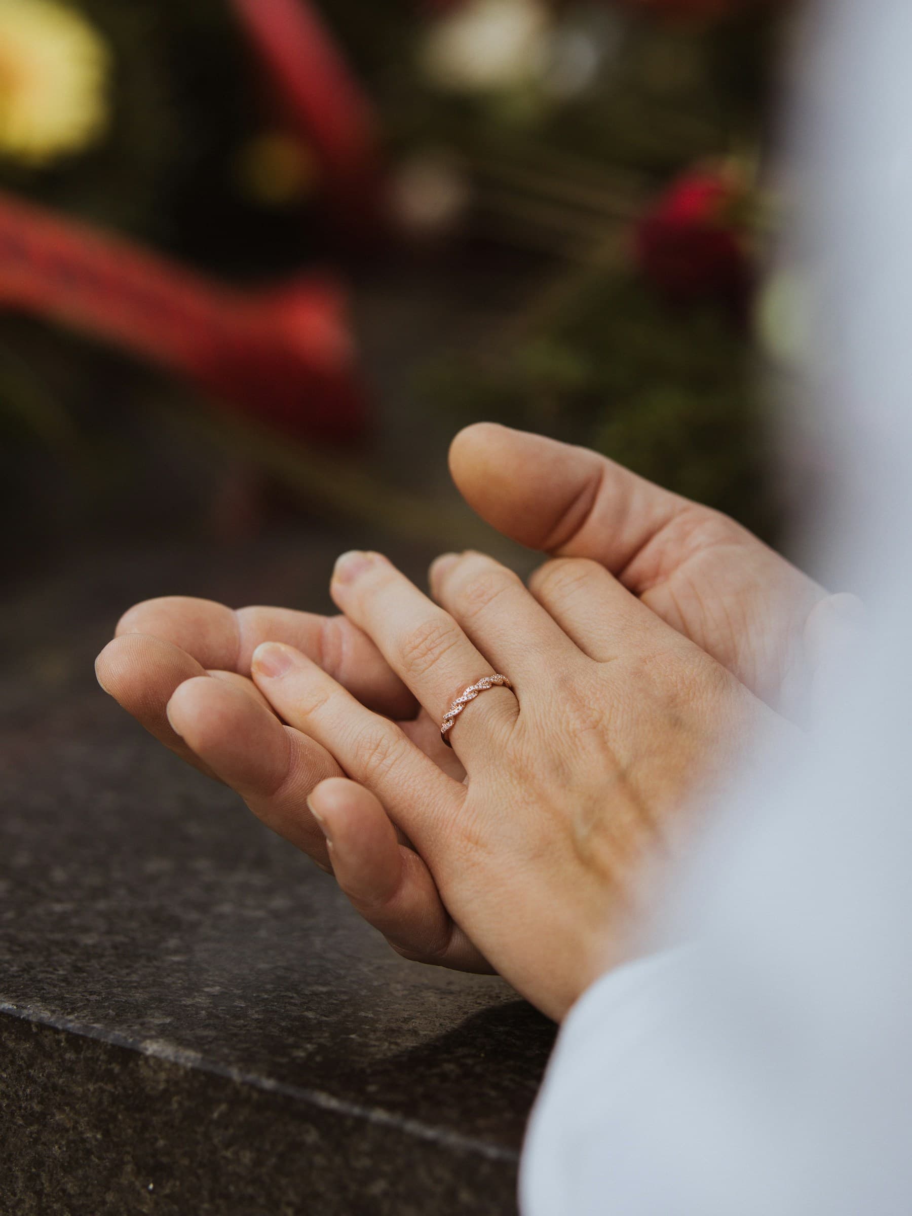 Two hands resting together over dark stone, one wearing a fine gold ring